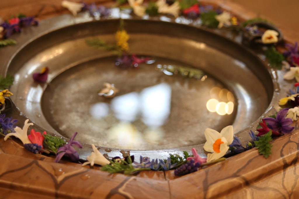 Mit Wasser gefüllter, geschmückter Taufstein